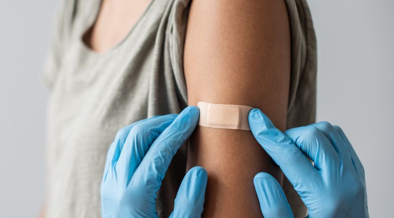 A health worker wearing gloves places a bandaid on a patient's upper arm following vaccination.