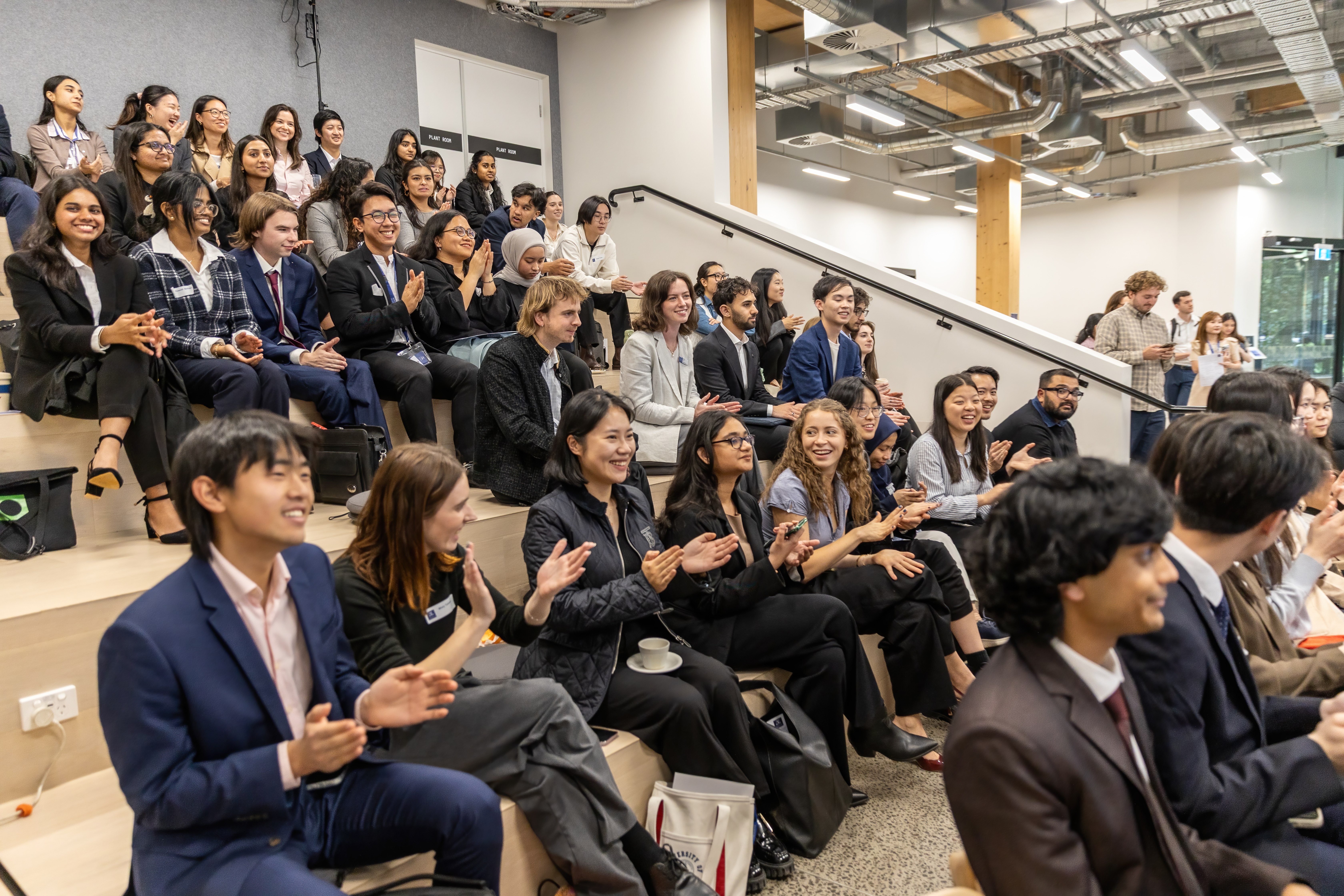 Some of the participating students pictured seated and applauding as winning teams are given certificates.