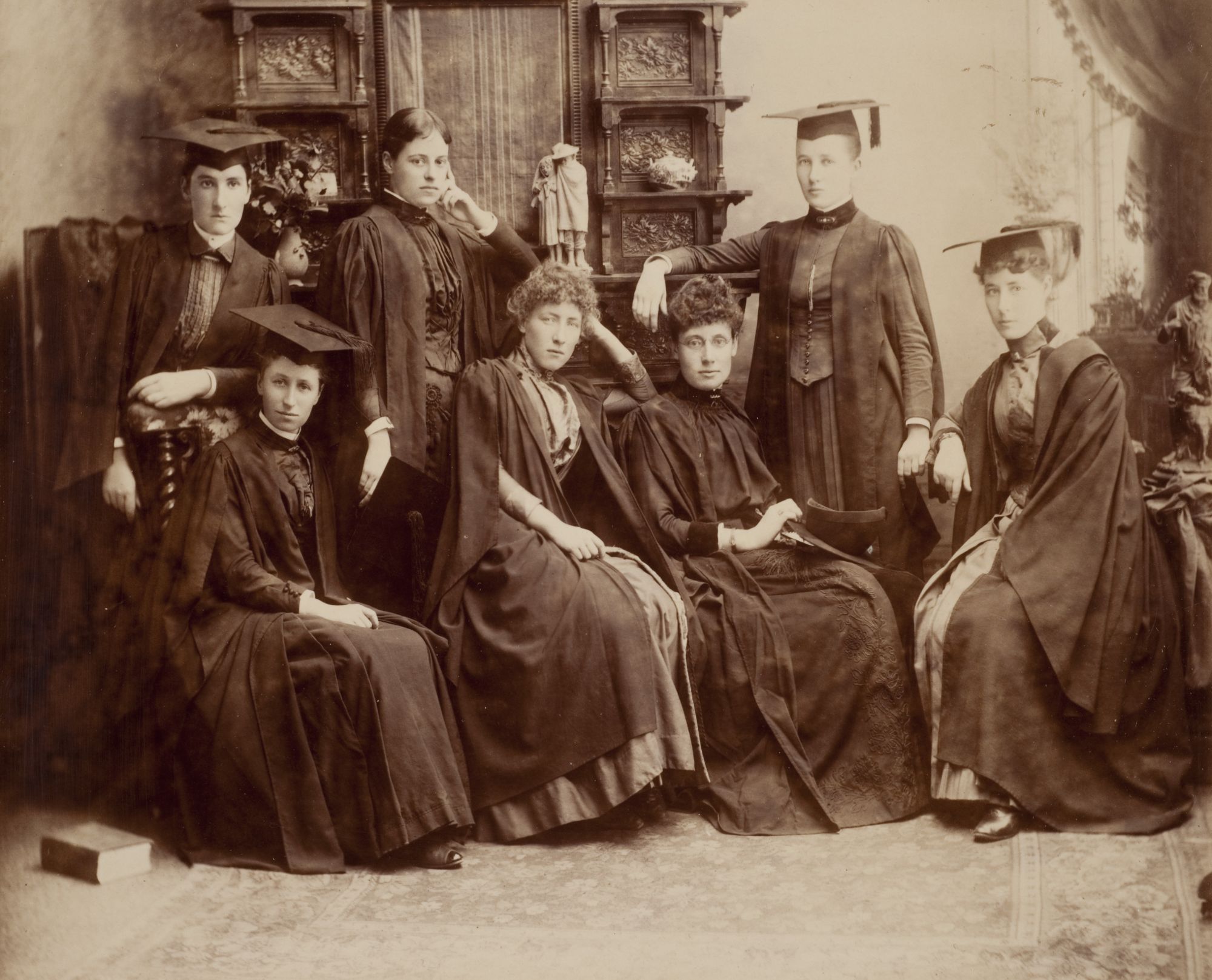 A black and white photograph of seven women, some wearing mortarboard caps, looking stern.