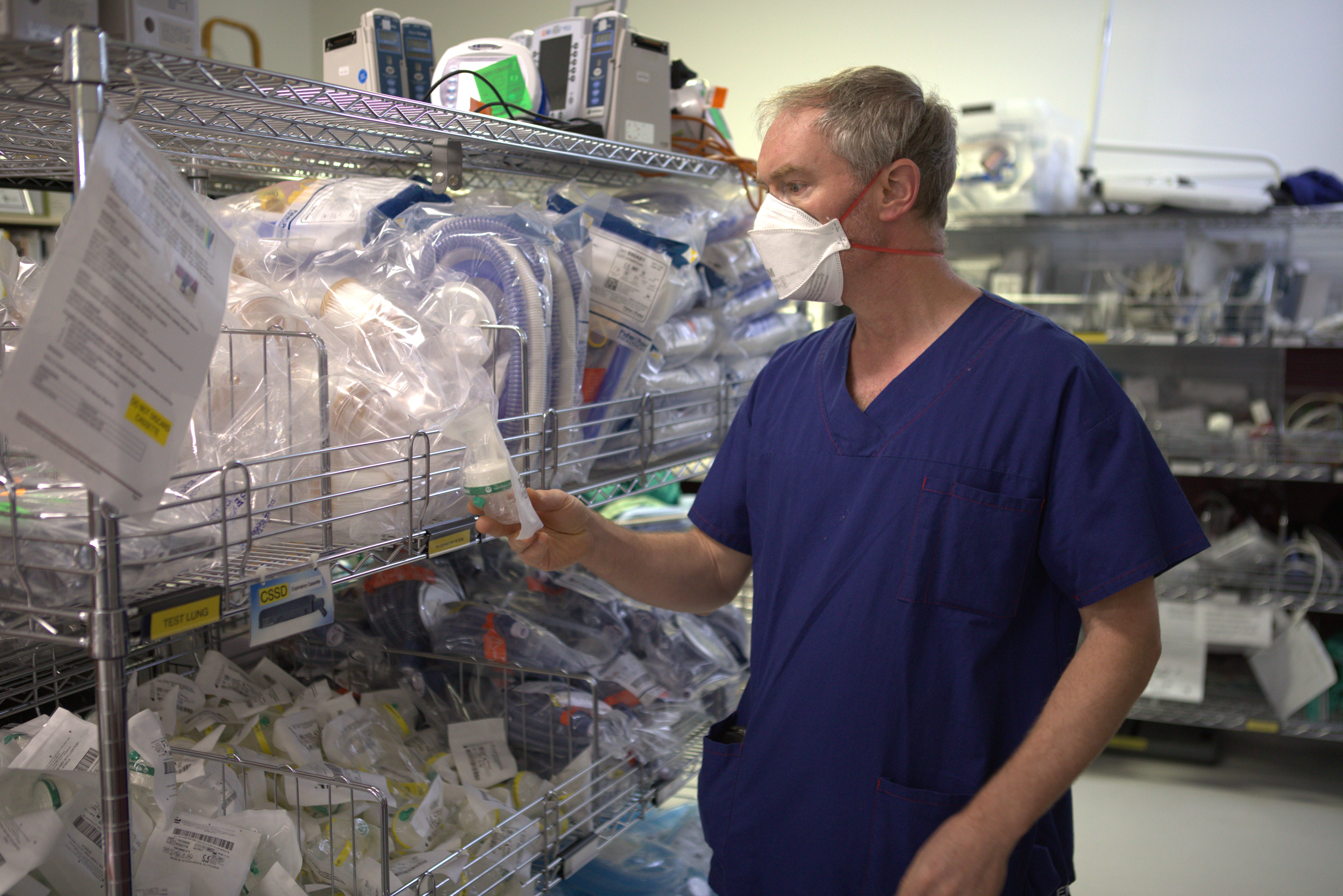 This is a photo of Professor Forbes McGain standing next to shelving unit full of medical one-time use equipment This is a photo of Professor Forbes McGain standing next to shelving unit full of medical one-time use equipment