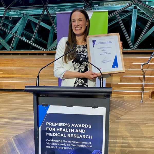 Dr Rachel Nelligan holding a framed certificate at the podium at the 2022 Premier's Awards ceremony, held at Federation Square