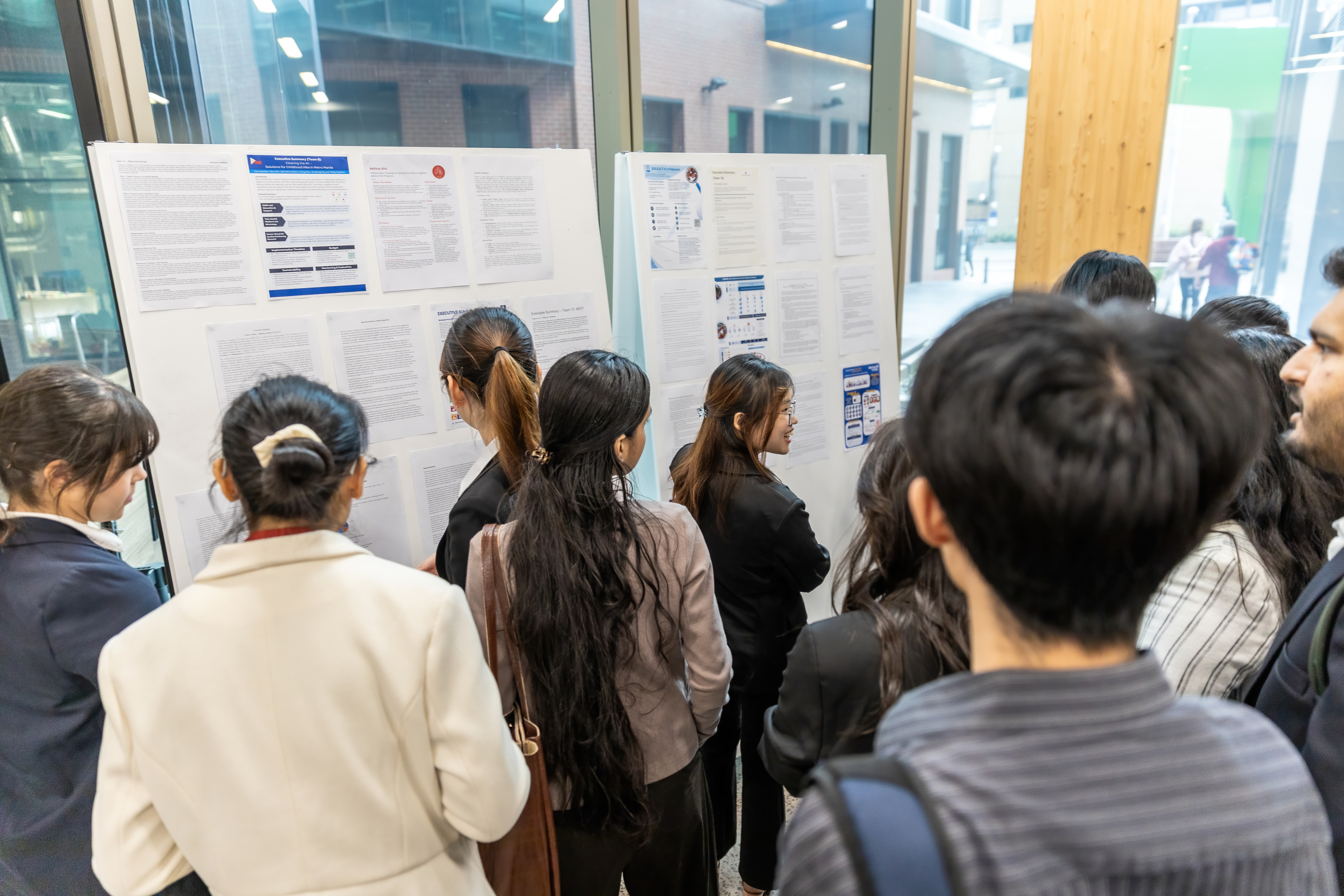 Students gathered near a noticeboard which displays printed copies of each team's proposal summary.