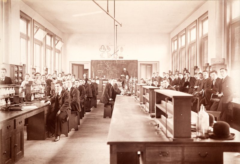 A first year physiology class in 1902. 10 women sit together on one side of the room, while many more male students make up the rest of the class.