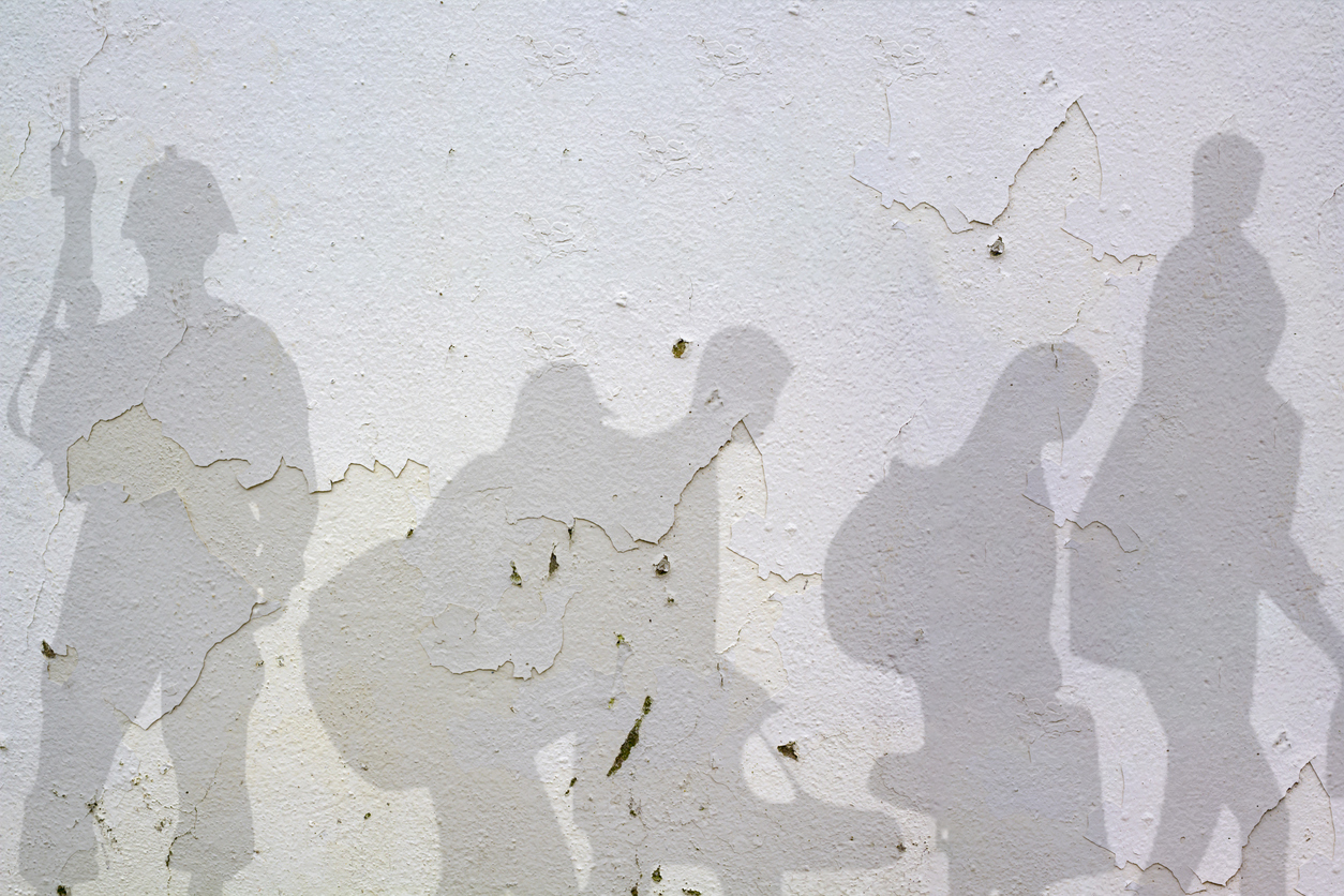 A wall with stripped paint, featuring shadows of a soldier carrying a gun, and a family carrying bags and other belongings - conveying the theme of forced displacement. 