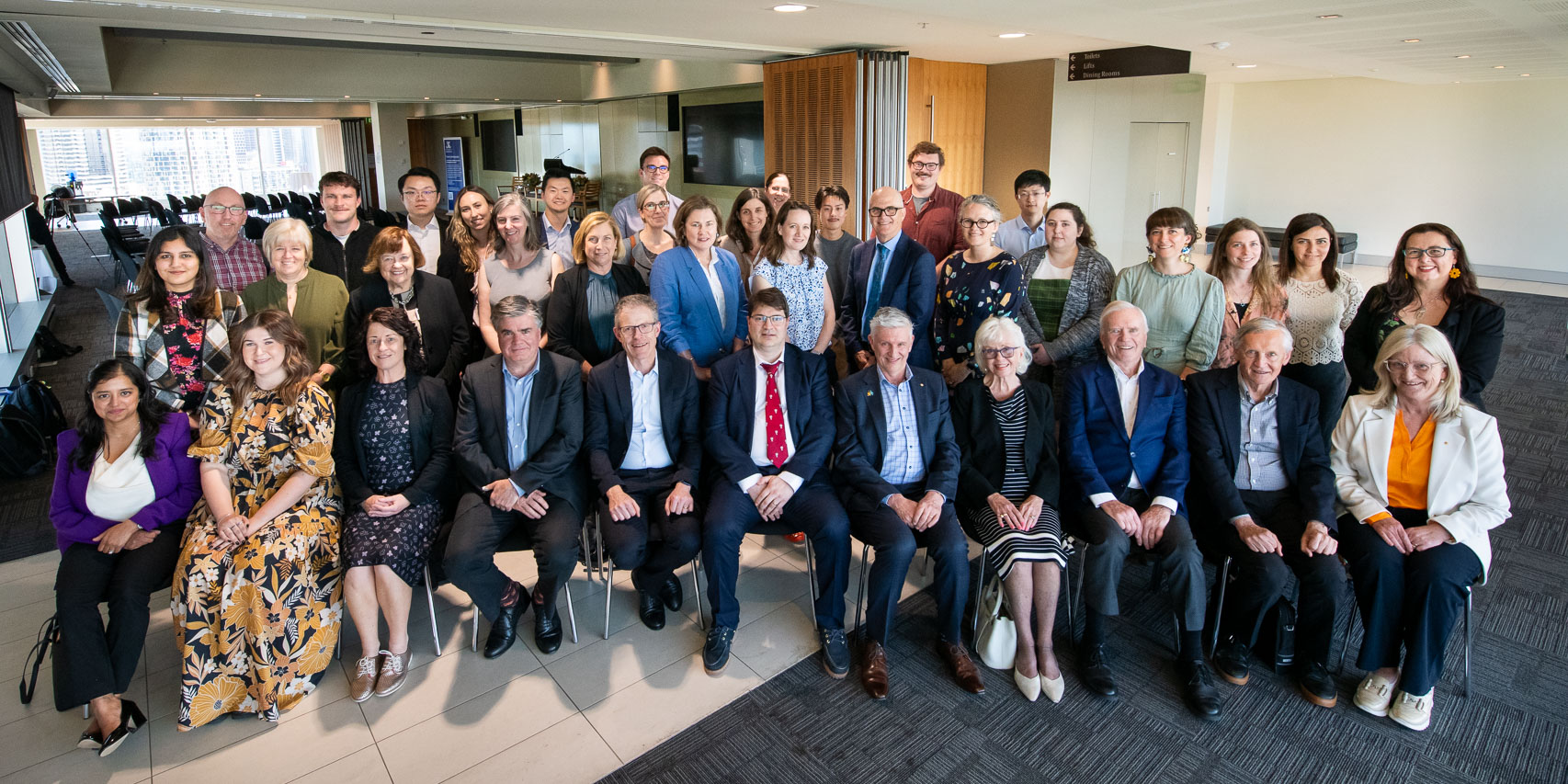 Attendees of the inaugural Galli Symposium seated for a group photo in a conference room facility. There are about 30-40 people in shot.