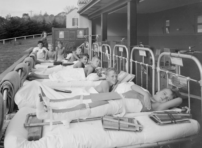 Children with polio lying in beds on an outdoor verandah at the Mt Eliza Orthopedic Section, c. 1936.