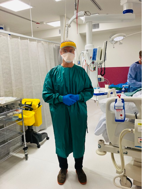 A critical care clinician in the critical care unit wearing a reusable gown. Around him are various pieces of medical equipment.