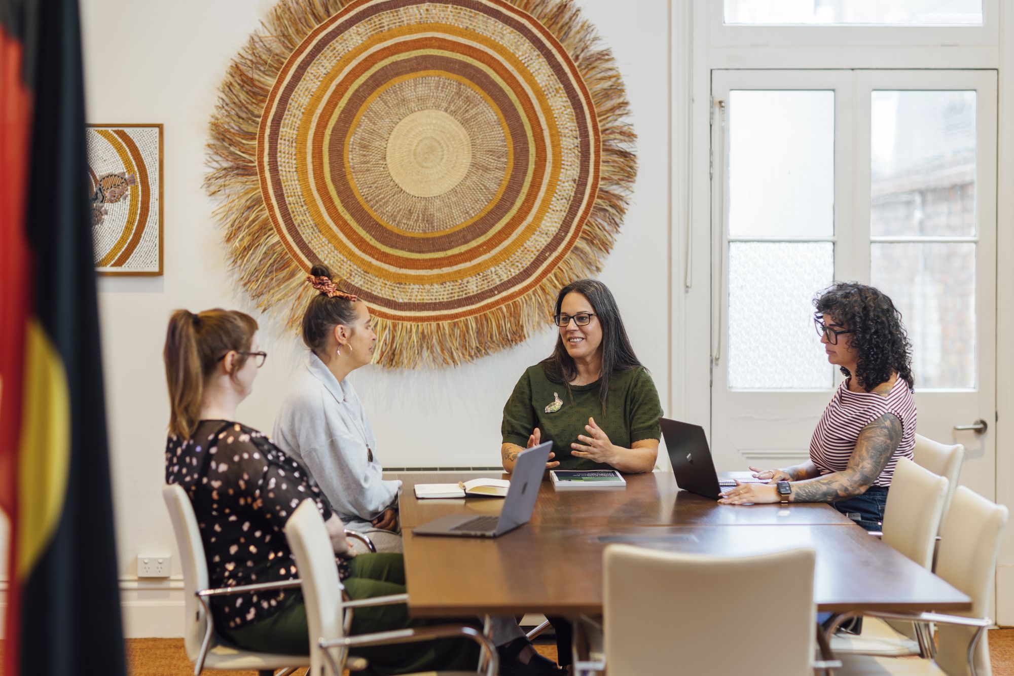 Dr Emily Munro-Harrison, Dr Tahlia Eastman, Professor Shawana Andrews and Magenta Highfield sit talking in the boardroom at the Melbourne Poche Centre for Indigenous Health.