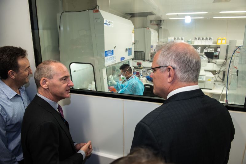 Dr Mike Catton, Senior Scientist Dr Julian Druce and then-Prime Minister Scott Morrison stand at a window overlooking a lab