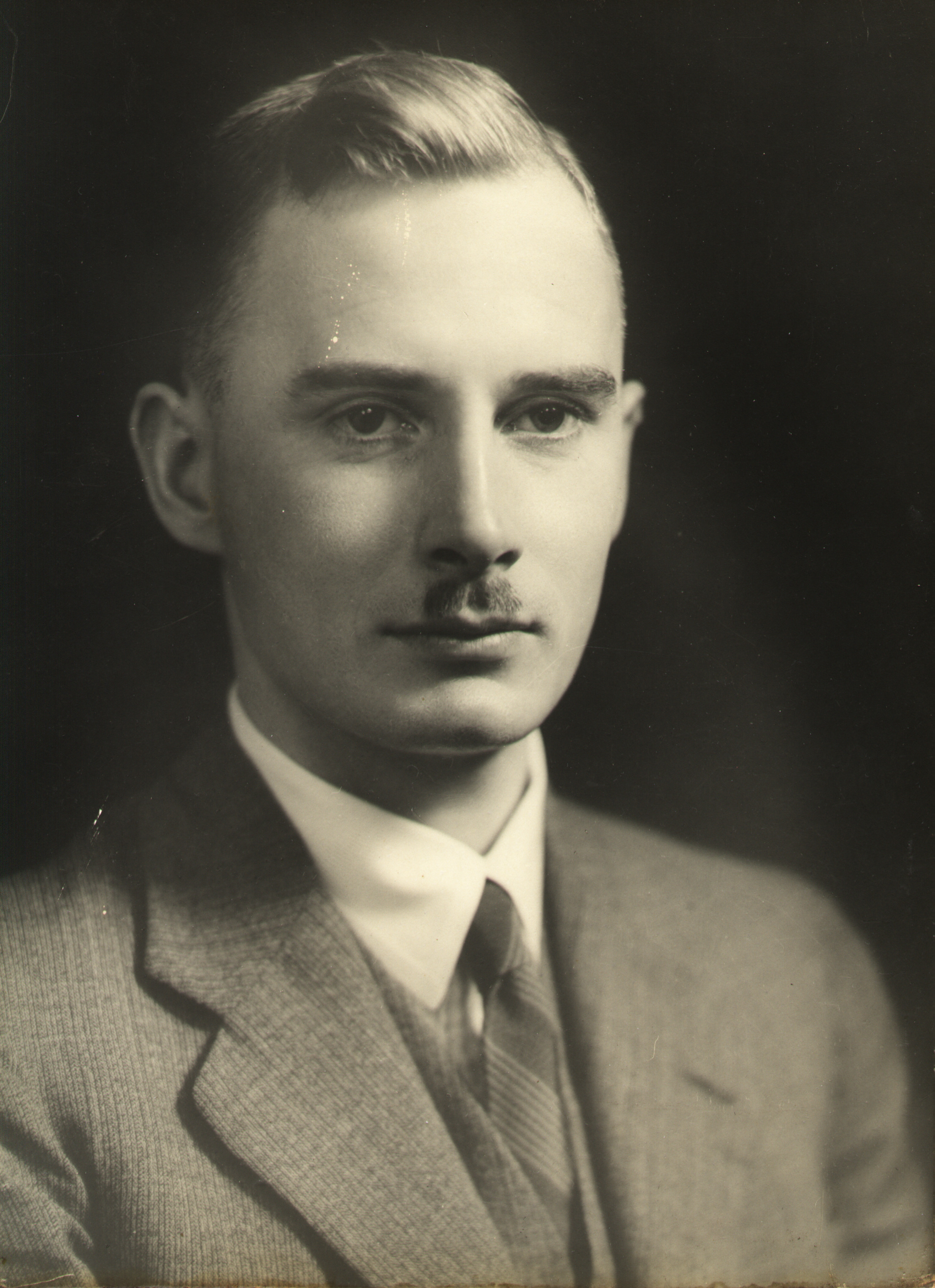A black and white photograph of a young man with a small mustache.