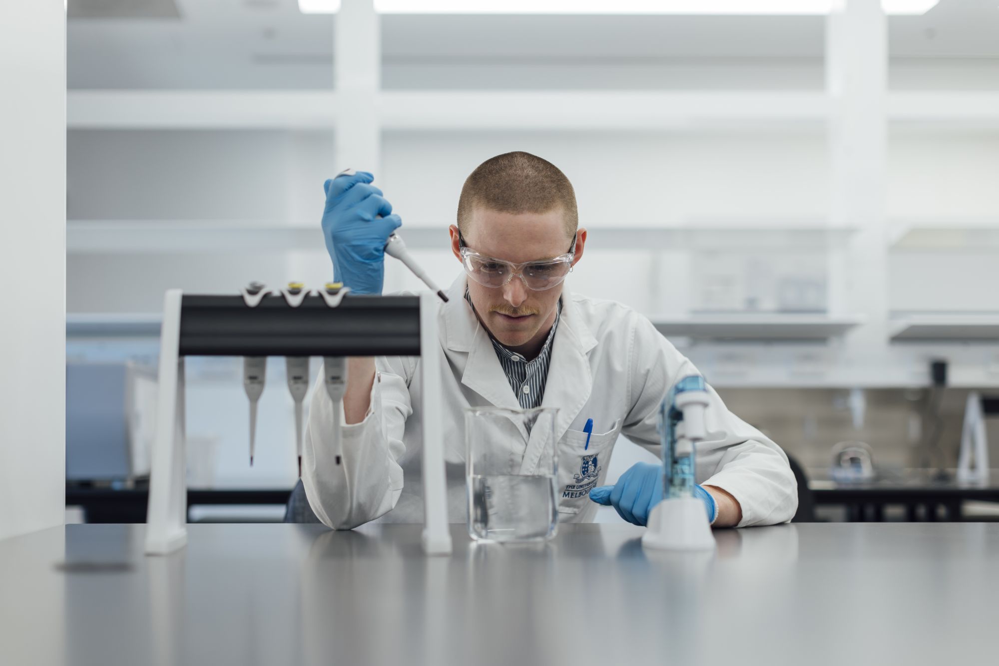 PhD student William Humble wears protective gear while using a pipette to add liquid to a beaker in the new ACMD laboratories.