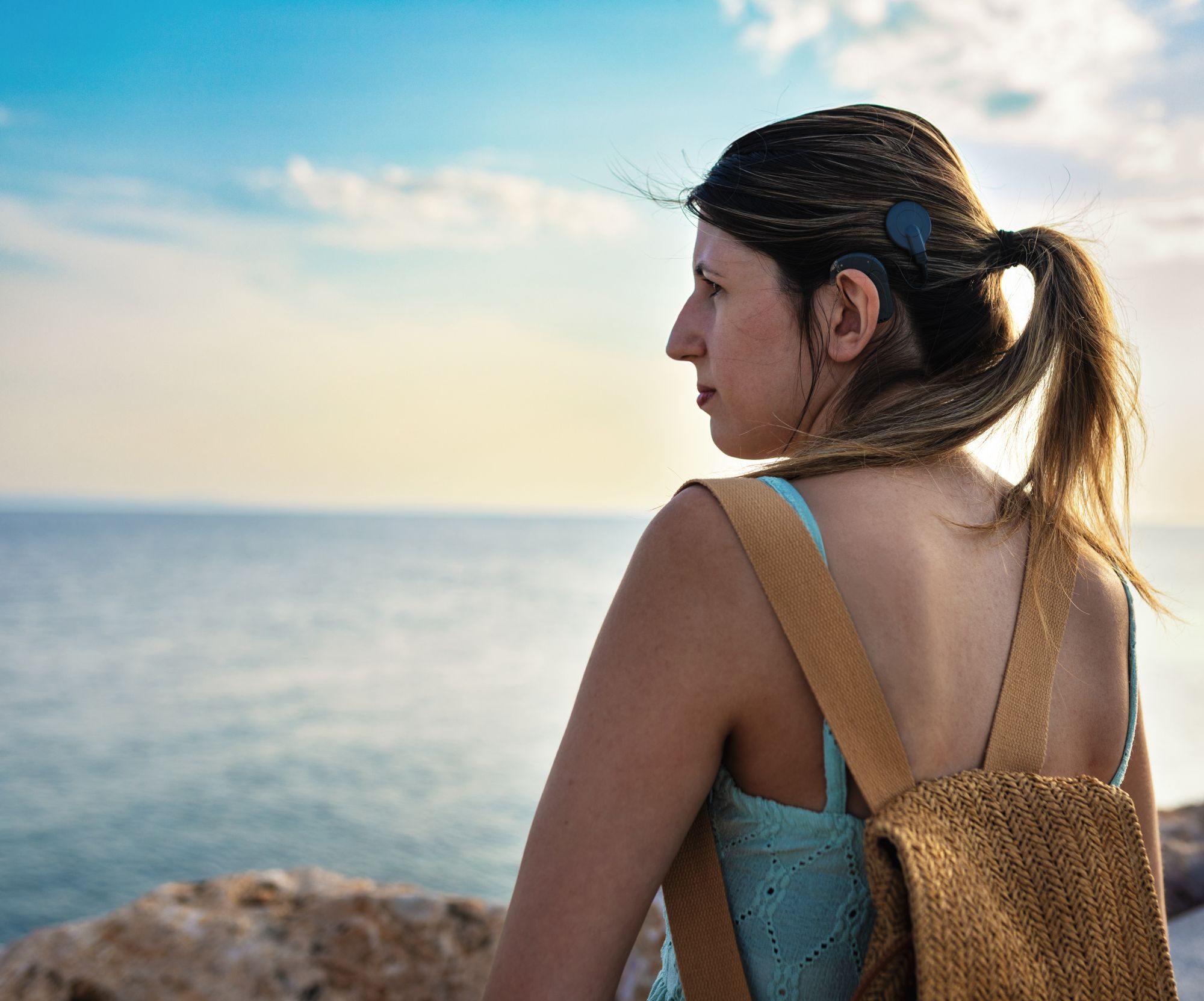 A young woman with a cochlear implant stands on a beach looking out over the horizon.