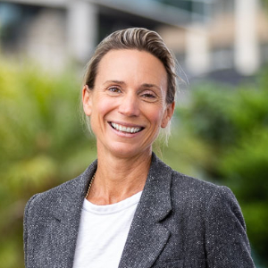 Image for Professor Liz Molloy smiling at the camera with an outdoor greenery background