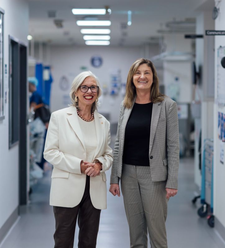 Alum Professor Kate Drummond AM and Professor Christobel Saunders AO smile in a hallway at the Royal Melbourne Hospital