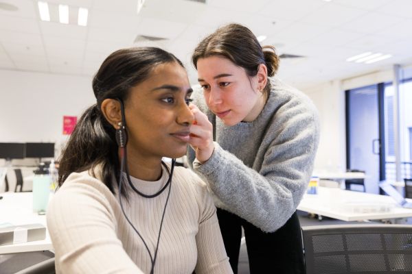Audiology student placing in hearing aid into her partner's ear