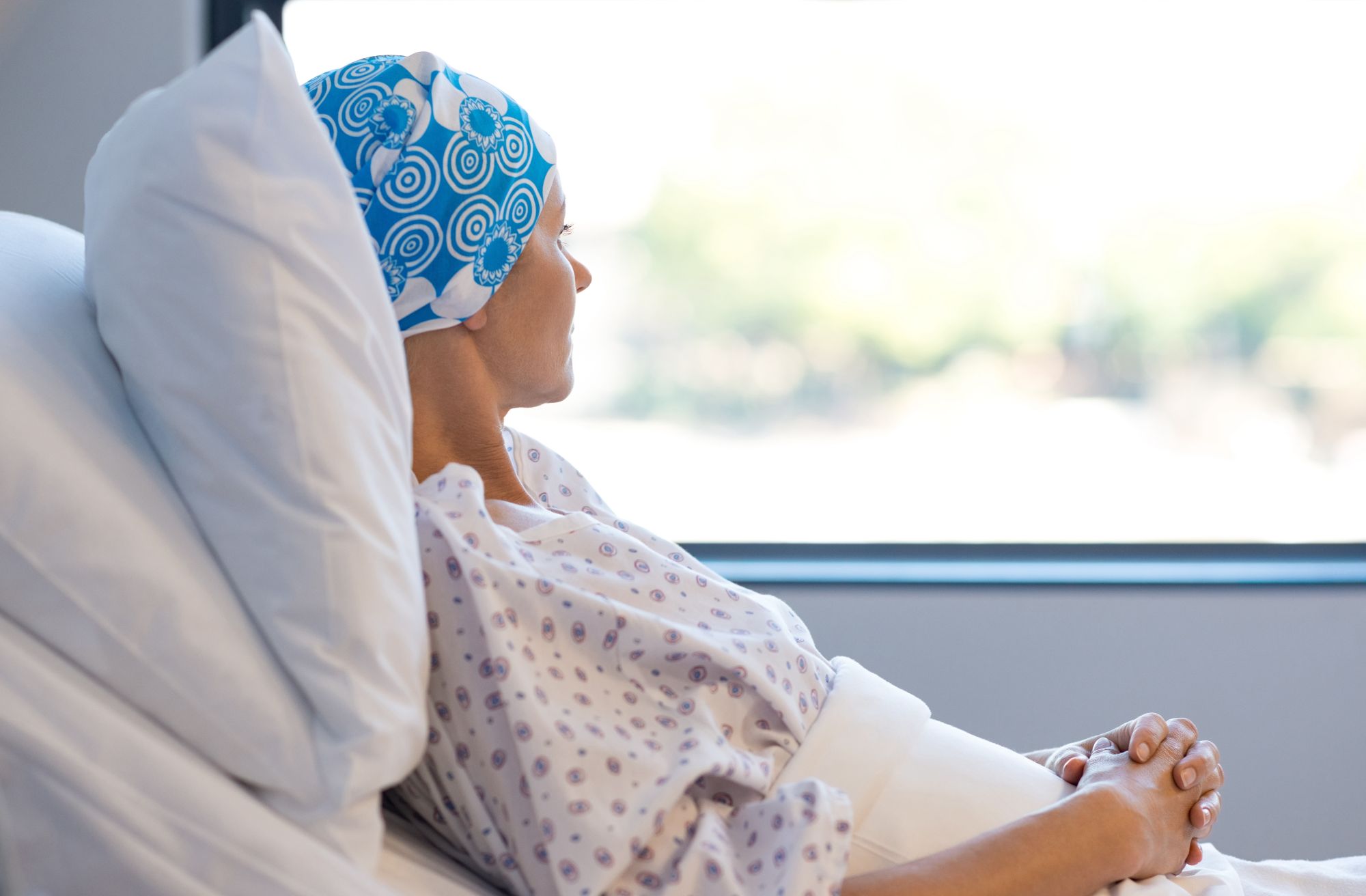A female cancer patient sits in a hospital bed looking out the window.
