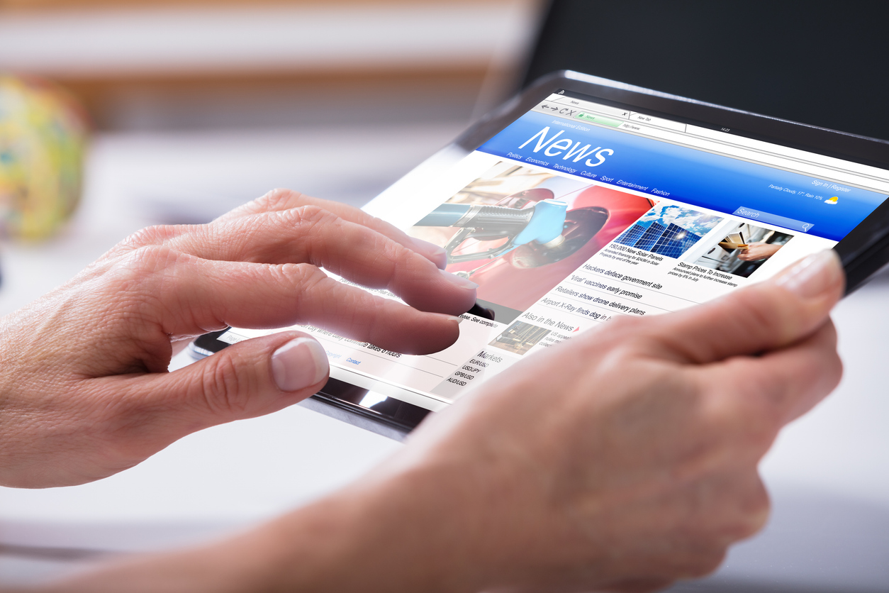 Image of large hands holding an iPad and scanning news.